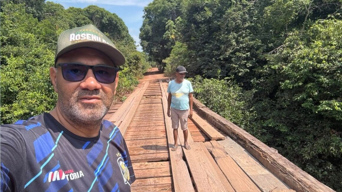 Vereador Rosenildo Freitas percorre comunidades de Tailândia em agenda itinerante O vereador Professor Rosenildo Freitas, de boné com seu nome e óculos escuros, tira uma selfie sobre uma ponte de madeira em área de vegetação na zona rural de Tailândia, com um morador ao fundo