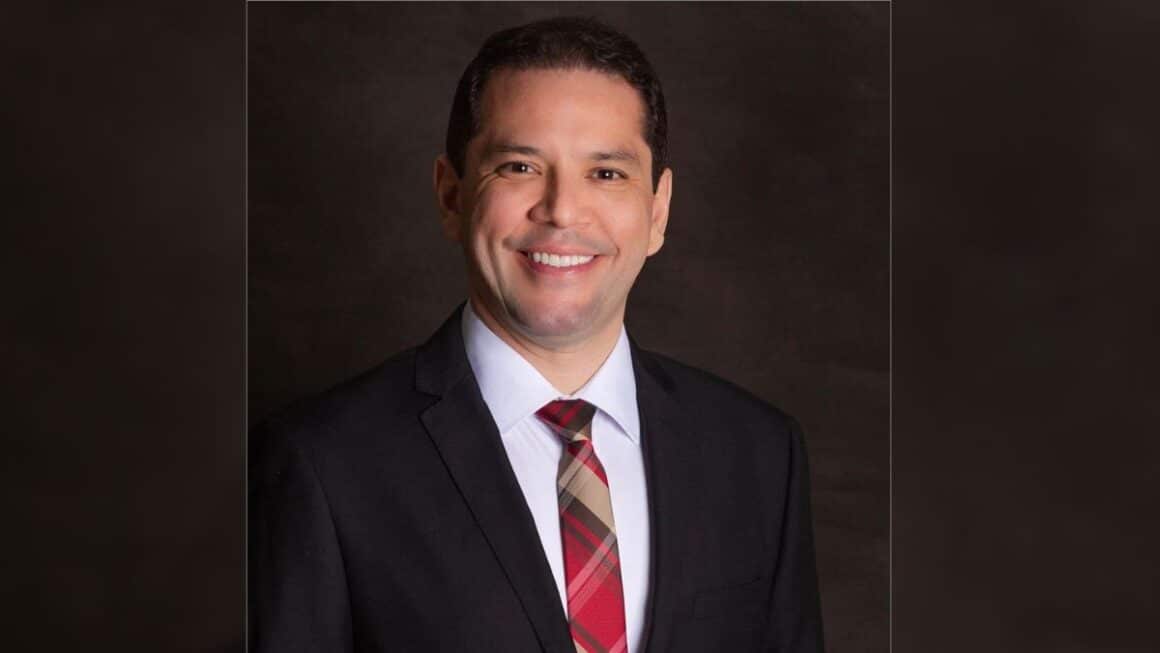 I Simpósio JusPará confirma advogado criminalista Tiago Brito entre os palestrantes Retrato profissional do advogado criminalista Dr. Tiago Brito, sorrindo de terno preto, camisa social branca e gravata vermelha xadrez sobre fundo escuro.