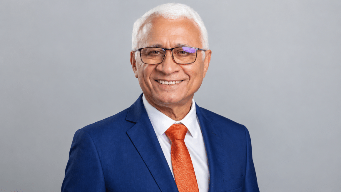 Gestão de Rubens Teixeira em Moju: obras, presença e resultados Retrato oficial do prefeito de Moju, Rubens Teixeira (MDB), sorrindo de terno azul-marinho, gravata laranja e óculos de grau sobre fundo cinza neutro.